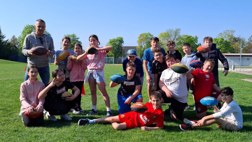 Schülerinnen und Schüler der NÖMS und PTS Ebreichsdorf posieren mit Flag-Football-Bällen auf dem Sportplatz, zusammen mit ihrem Trainer