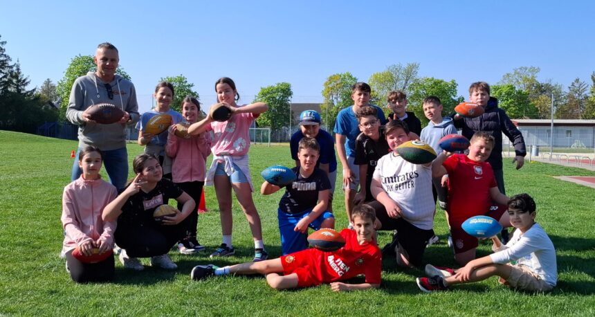 Schülerinnen und Schüler der NÖMS und PTS Ebreichsdorf posieren mit Flag-Football-Bällen auf dem Sportplatz, zusammen mit ihrem Trainer