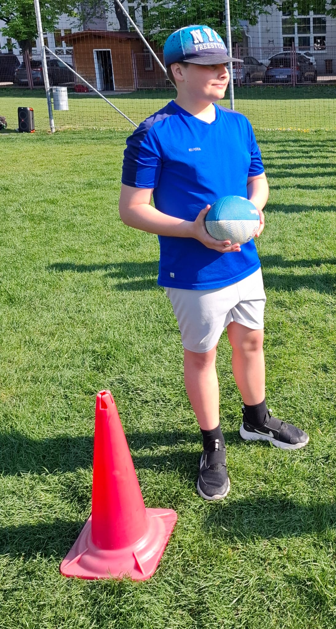 Schüler in blauem Trikot und Cap hält einen Football am Sportplatz