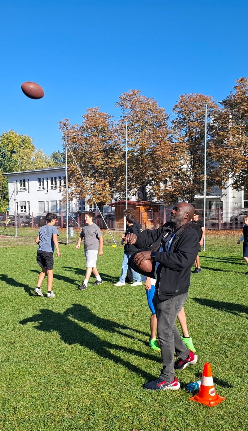 Der Coach fängt einen Football, ein zweiter Ball fliegt hoch am blauen Himmel