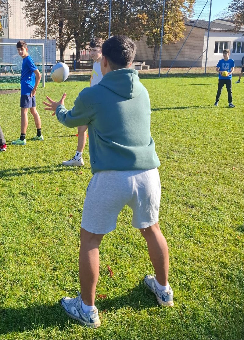 Ein Schüler im grünen Pullover fängt einen Ball, andere Schüler beobachten ihn