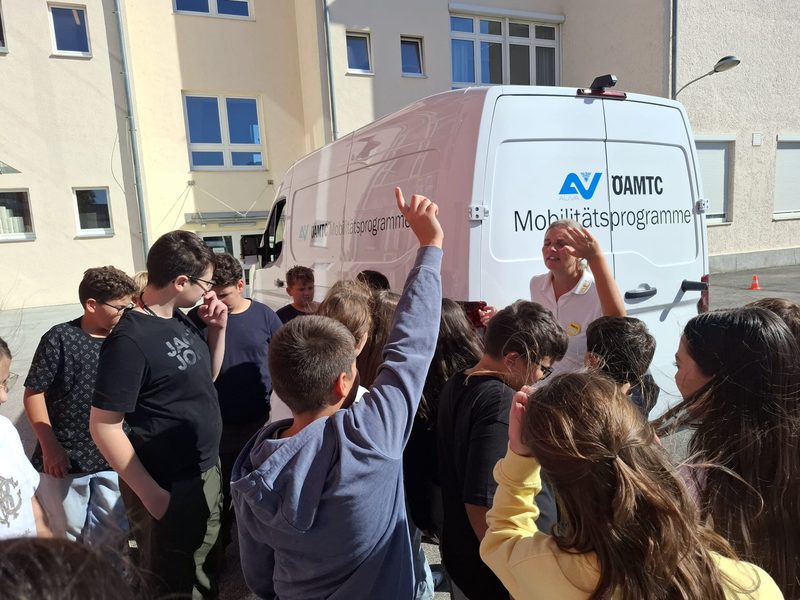 Schüler:innen stehen im Halbkreis vor dem ÖAMTC-Bus, eine Schülerin zeigt auf